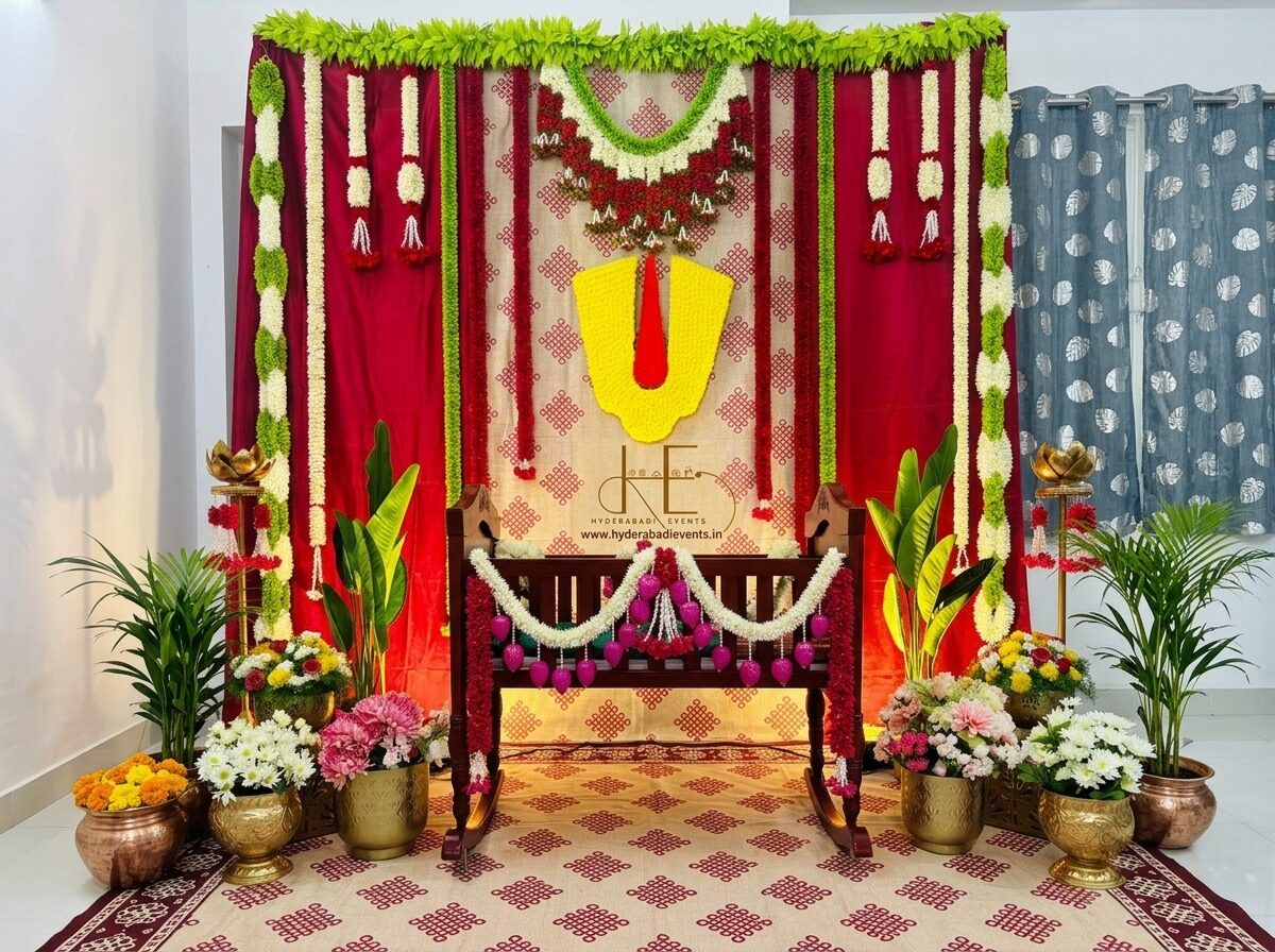 Red and green cradle ceremony decoration with floral garlands, traditional backdrop and wooden cradle setup.