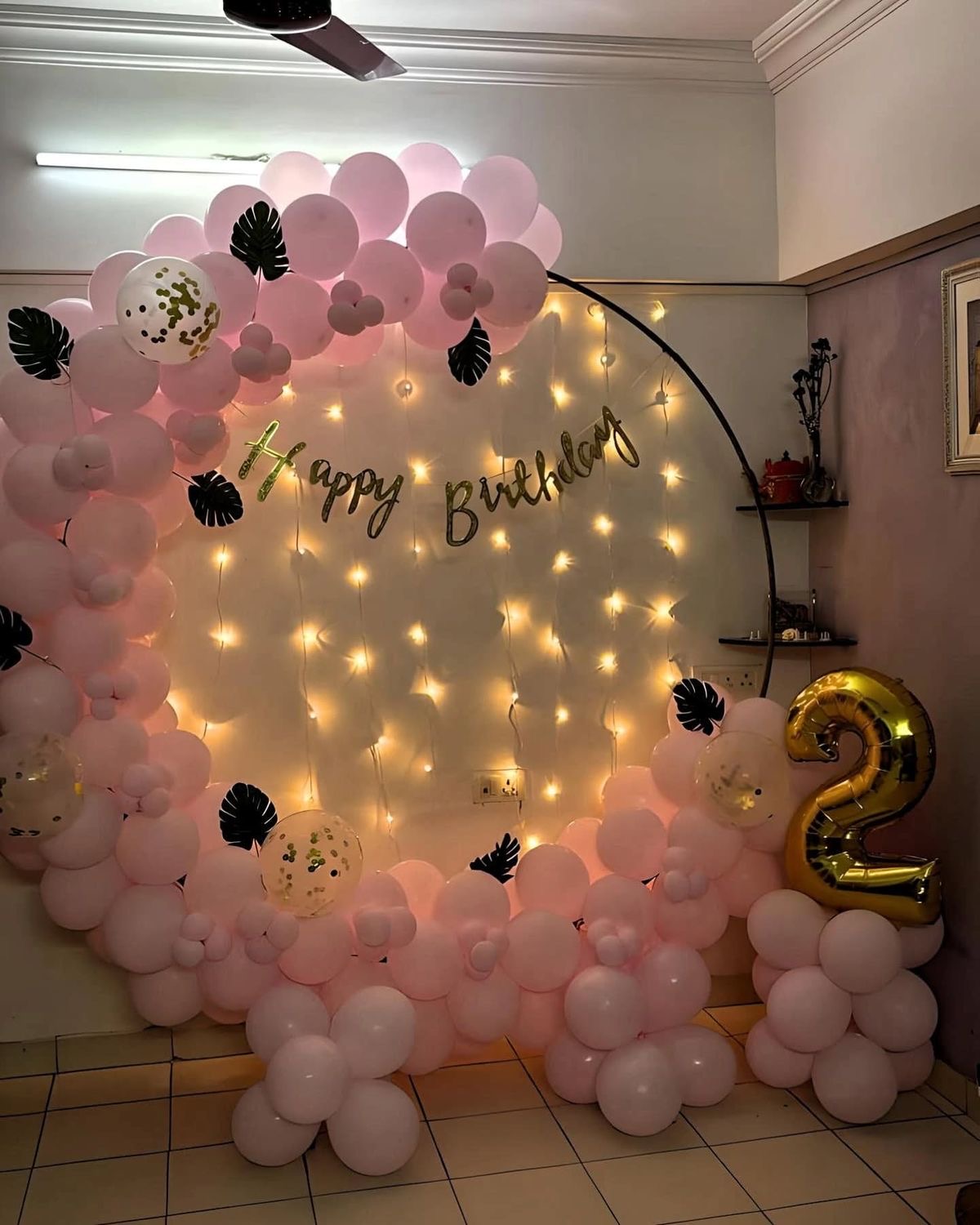 Pastel pink balloon ring birthday decoration with warm fairy lights backdrop and golden number balloon