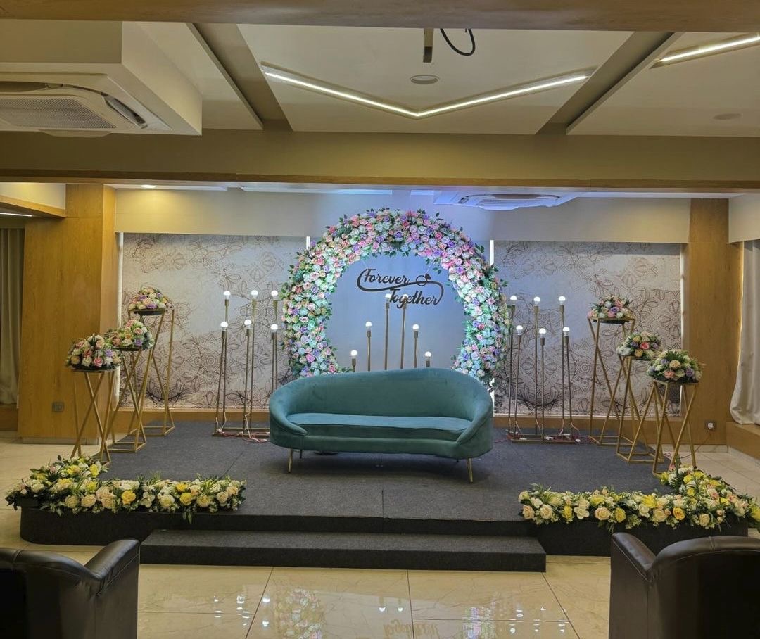 Round floral ring reception stage with pastel flower arch, candle stands and teal sofa seating arrangement.