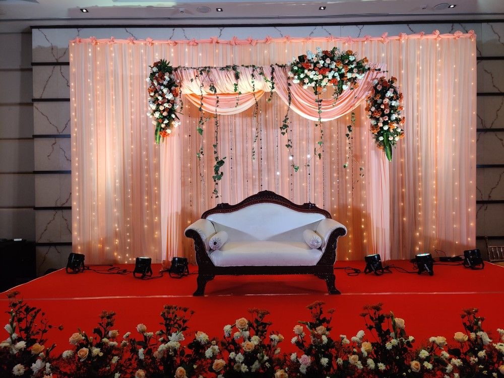 Premium white floral wedding reception stage decoration with luxury draping backdrop, designer flower arrangements and modern couple sofa.