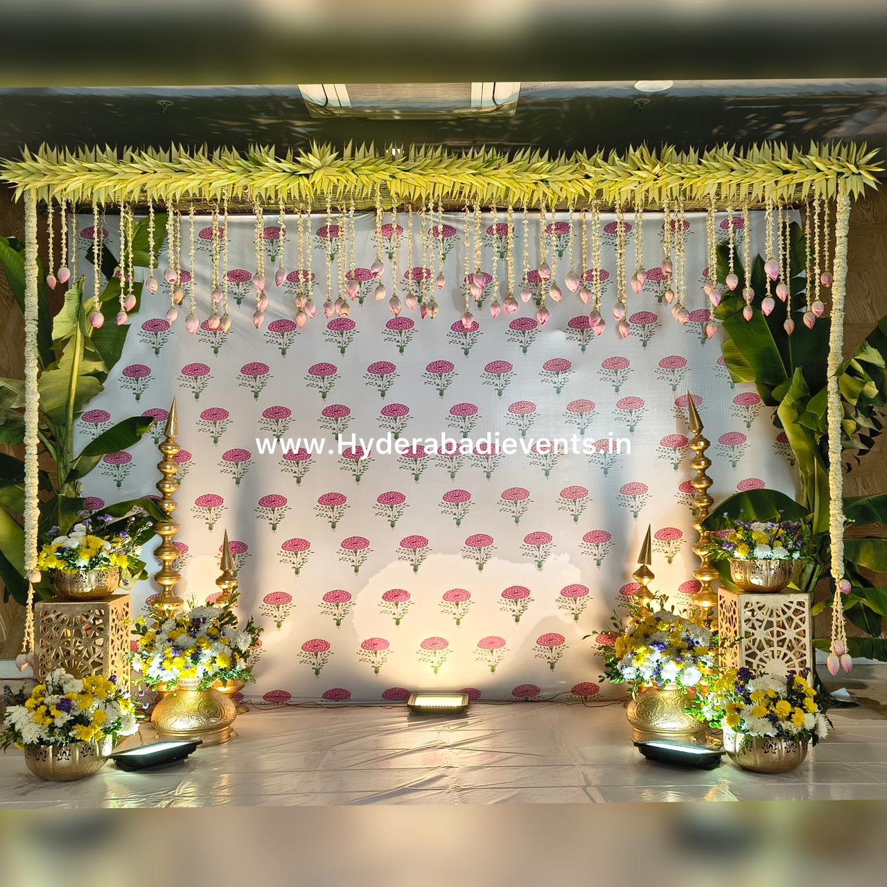 Minimal traditional backdrop with floral hangings, banana leaves and brass decor.