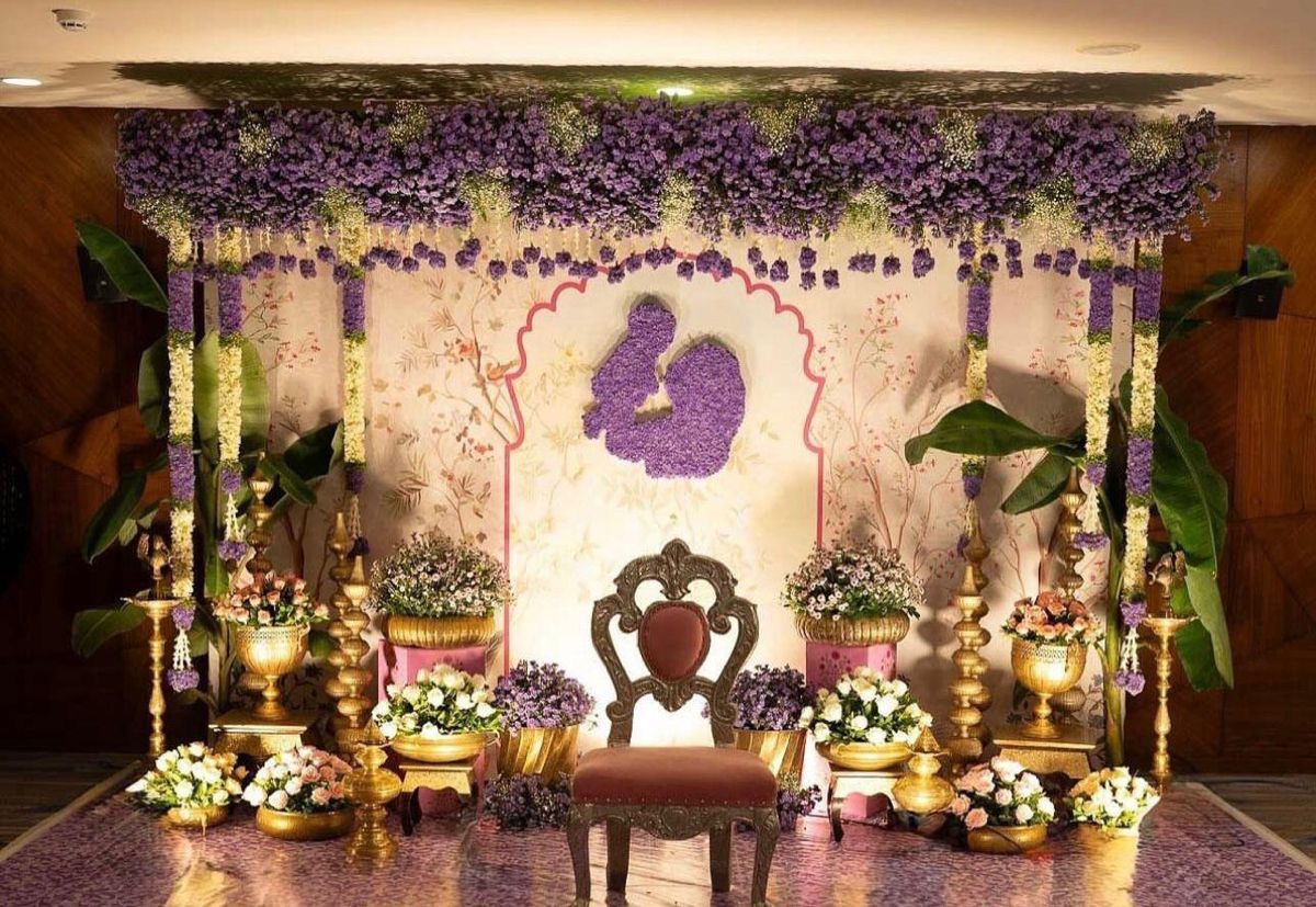 Luxury baby shower decoration with purple floral canopy, gold props and elegant seating stage.