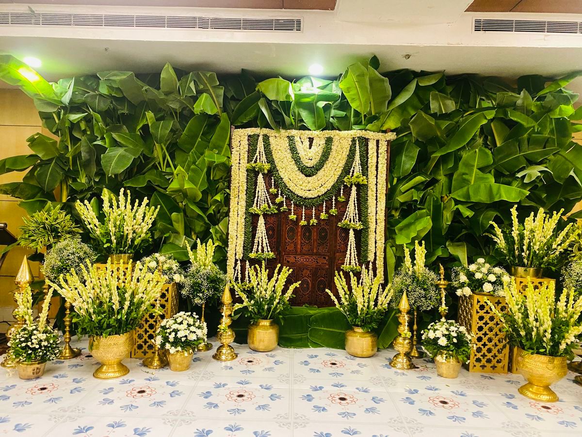 Banana leaf backdrop decoration with white floral garlands and brass pots for traditional events.