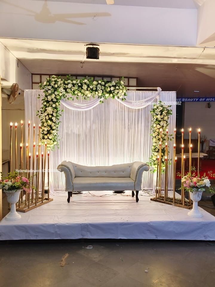Elegant white floral stage decoration with candle stands, green foliage and luxury sofa seating.