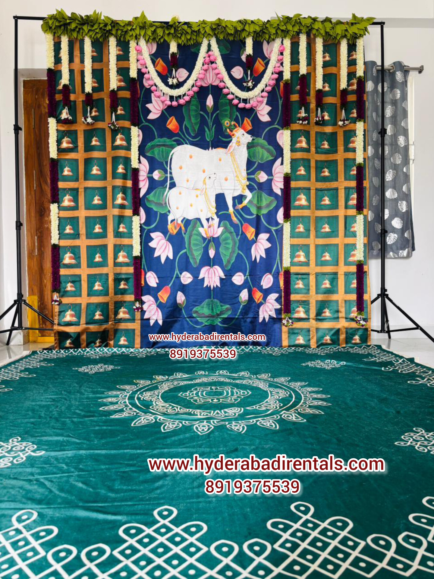 Traditional cow lotus theme backdrop rental with floral garlands and green rangoli floor setup for pooja and housewarming events in Hyderabad.