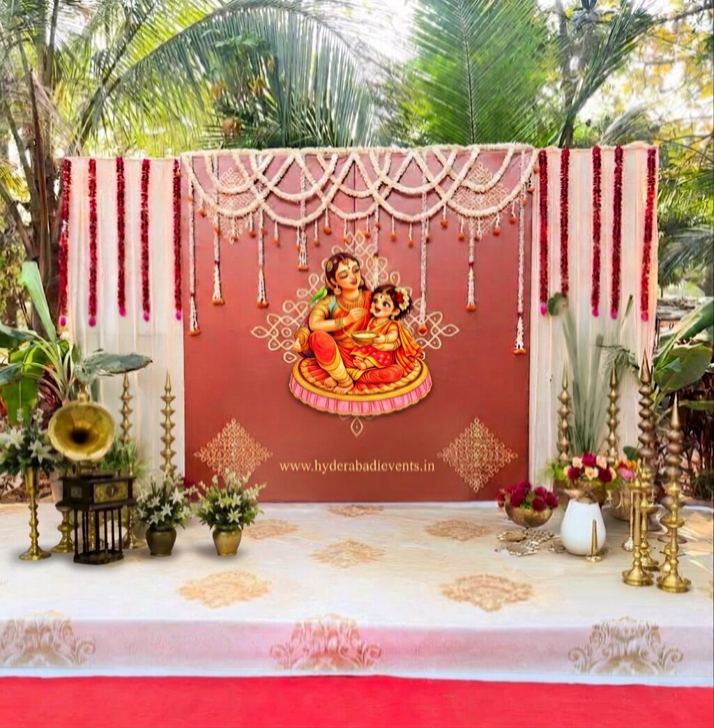 Traditional mother and baby naming ceremony backdrop decoration with floral garlands, white drapes, brass lamps, flower arrangements, and elegant South Indian stage decoration in Hyderabad.