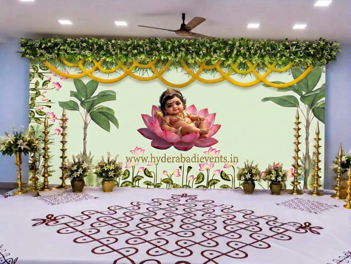 Baby Krishna naming ceremony decoration with lotus backdrop, banana leaf artwork, floral garlands, brass lamps, rangoli floor design, and premium traditional cradle ceremony stage decoration in Hyderabad.
