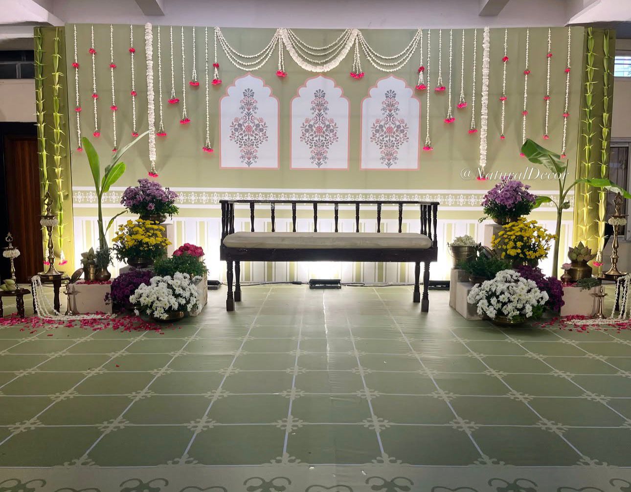 Premium sage green Seemantham stage decoration with jasmine hanging garlands, floral backdrop, wooden seating and South Indian baby shower décor.