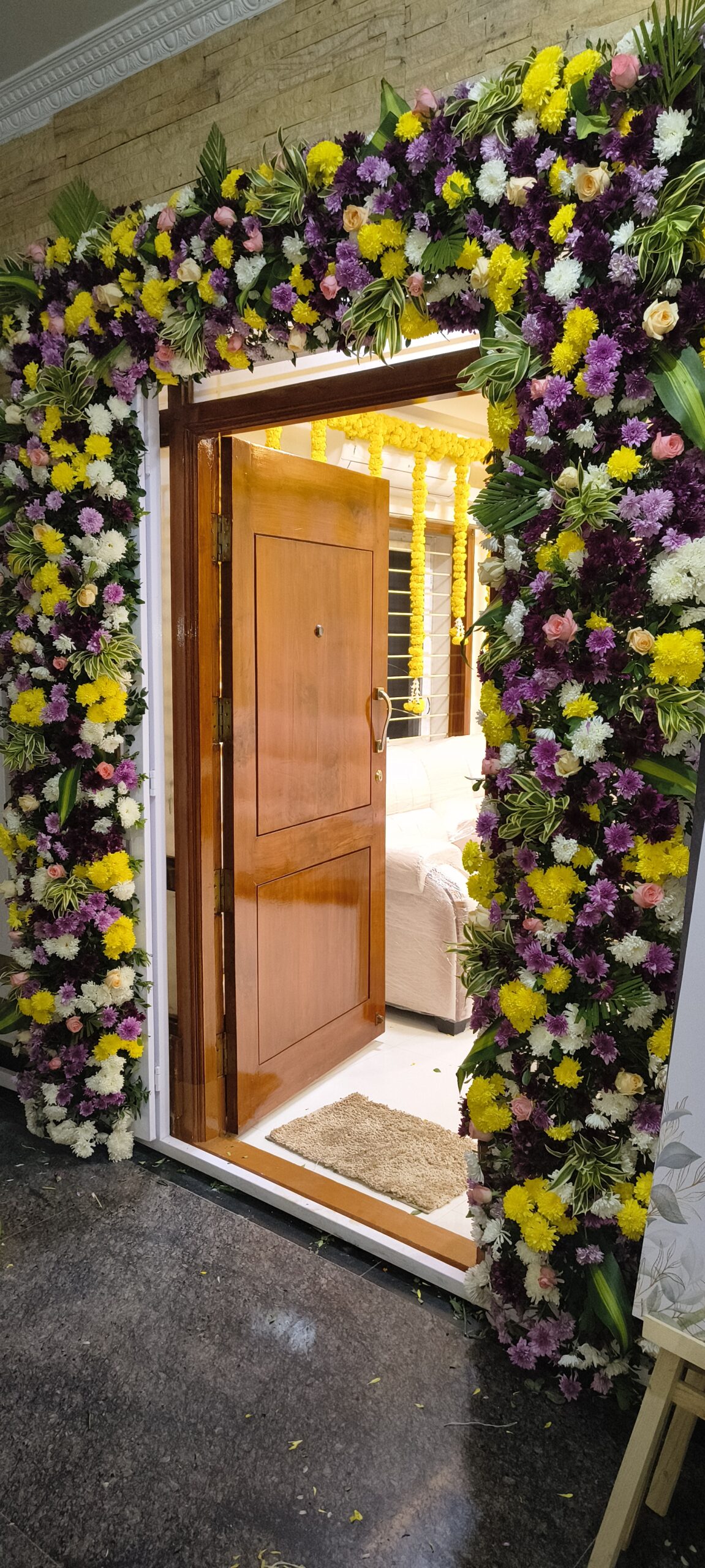 Elegant house entrance flower decoration with fresh chrysanthemums, roses, tropical leaves, and floral doorway arch for housewarming, weddings, and traditional ceremonies in Hyderabad.