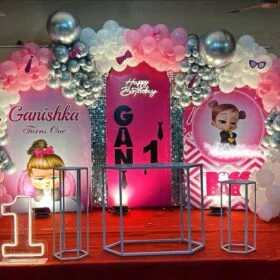 Boss Baby-themed 1st Birthday Party Decoration Kit with pink, white, and silver balloon garland, LED "1" number, themed backdrop panels, and decorative pedestals.