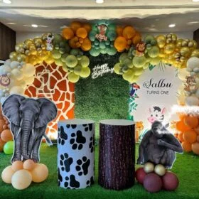 Jungle Safari-themed 1st Birthday Party Decoration Kit featuring balloon arch, animal cutouts (elephant, gorilla), jungle grass carpet, personalized backdrop, and display pedestals.
