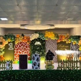 Deluxe Jungle Safari-themed 1st Birthday Party Decoration Kit featuring balloon arch, animal cutouts (gorilla, giraffe, zebra), personalized backdrop, display pedestals, photo display tree, and jungle grass carpet.