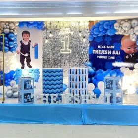 Boss Baby-Themed 1st Birthday Decoration Kit with personalized photo display, balloon arch in blue and silver, LED name lights, themed backdrop, info board, and shiny sequin curtain.